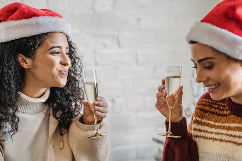 Cheerful ethnic women drinking champagne during Christmas celebration