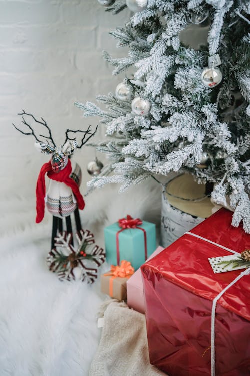 Free High angle many wrapped gift boxes and decorations placed on white fluffy carpet underneath Christmas tree during festive holidays Stock Photo