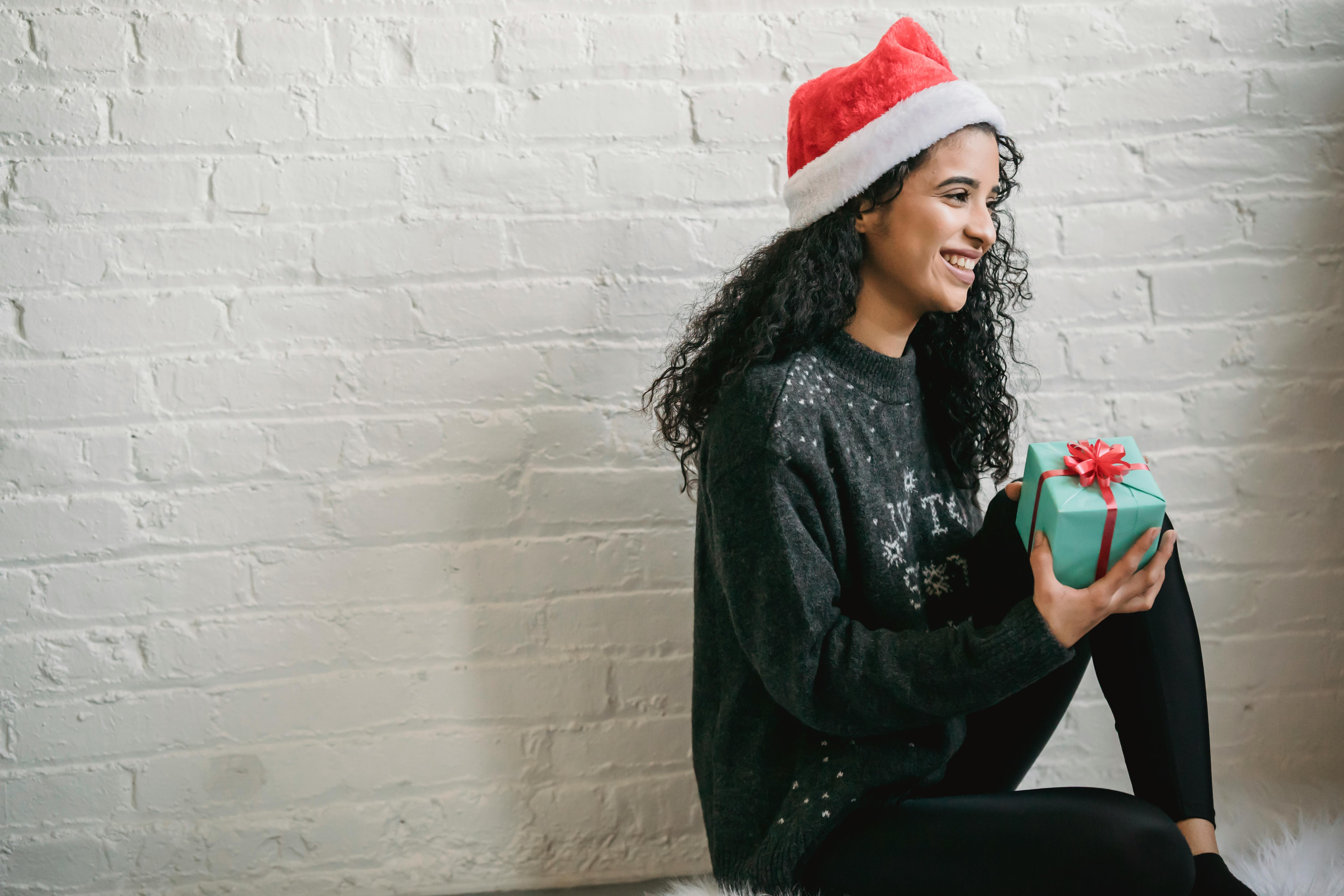 satisfied ethnic woman in santa hat with gift box