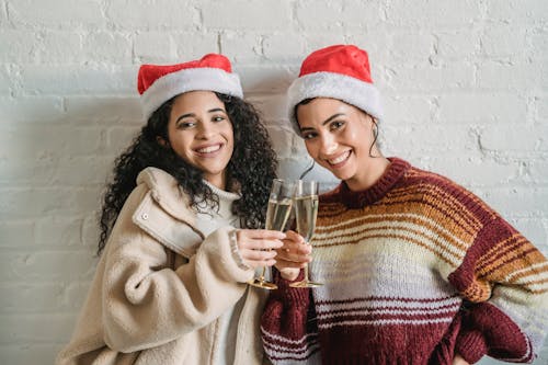 Happy ethnic women in Santa hats clinking champagne glasses