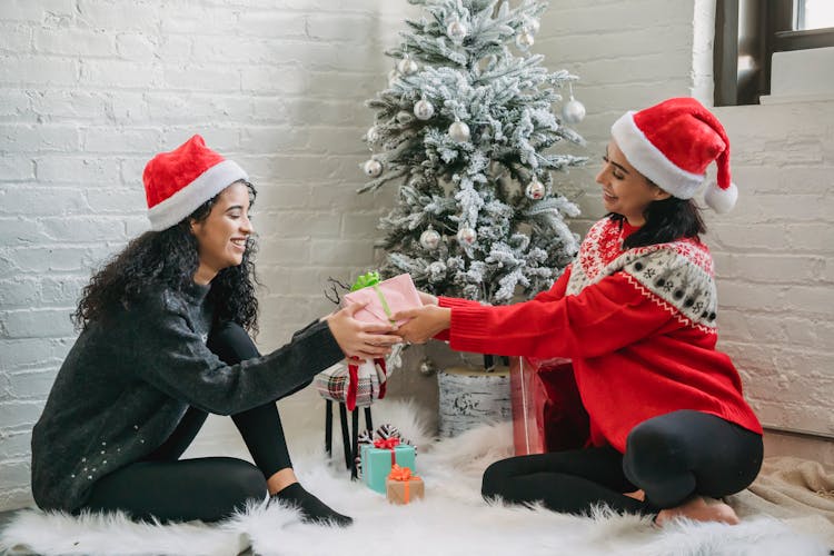 Happy Ethnic Female Friends Exchanging Gifts Under Christmas Tree