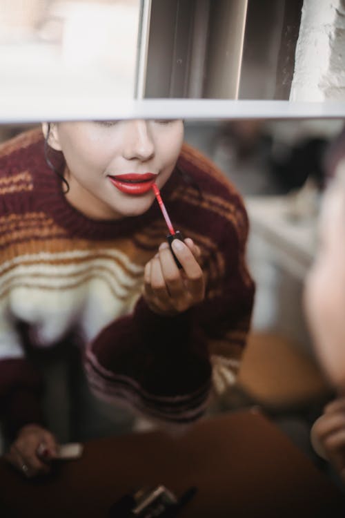 Crop female reflecting in mirror and applying makeup while preparing for occasion at home