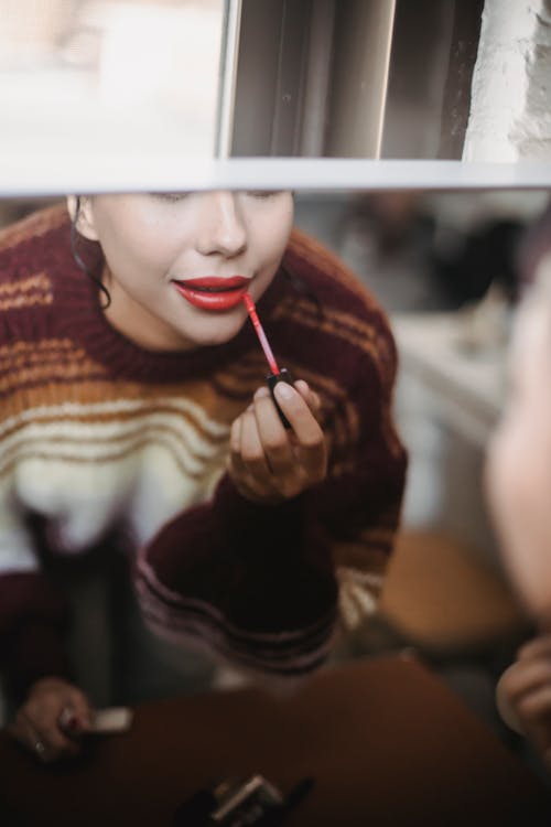 Free Crop female reflecting in mirror and applying makeup while preparing for occasion at home Stock Photo