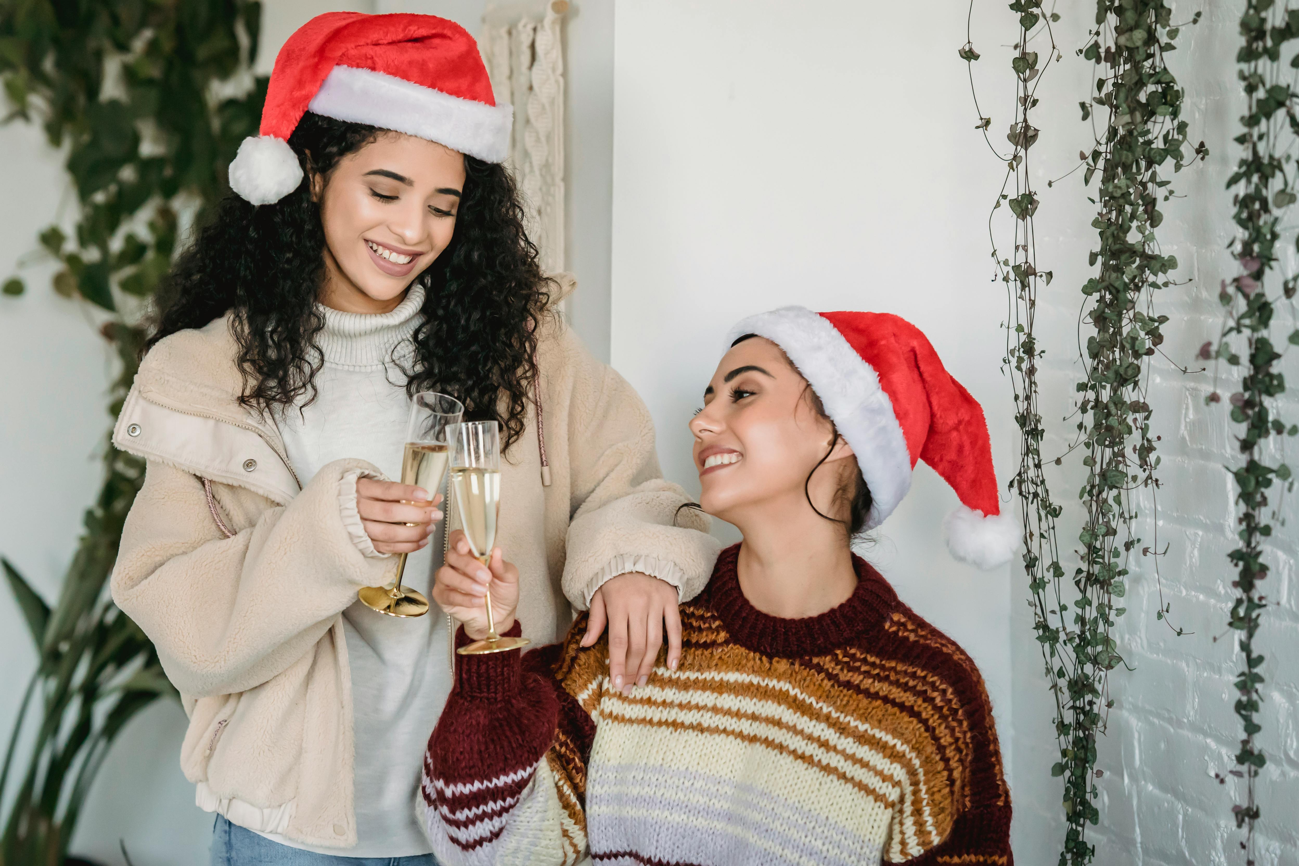 Two women celebrating with champagne, wearing Santa hats during a festive holiday gathering.