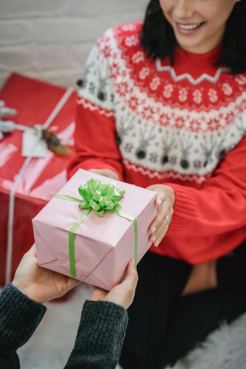 Free From above of crop smiling woman in sweater getting present for New Year celebration from friend Stock Photo