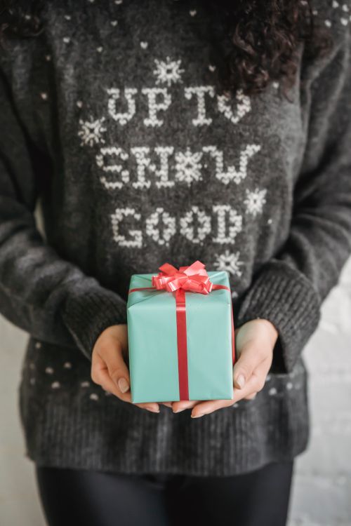 Free Crop anonymous female in warm sweater demonstrating gift box with ribbon for New Year holidays Stock Photo