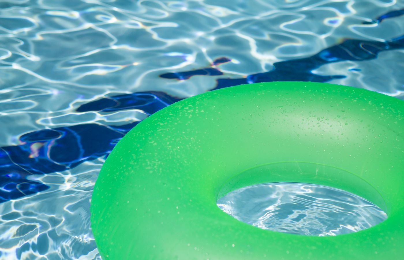 A vibrant green inflatable swim ring floating in a refreshing blue swimming pool.
