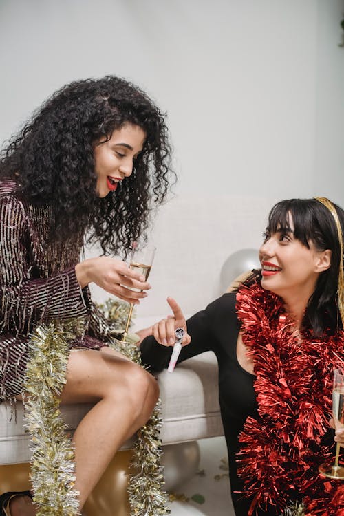 Positive ethnic females drinking champagne at Christmas party