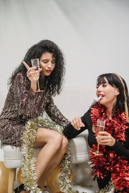 Woman with glass of champagne got drunk during New Year celebration with friend blowing party horn