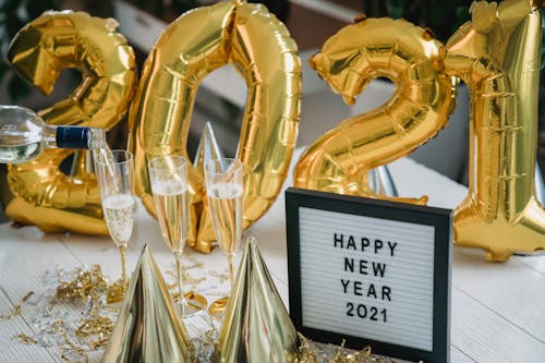 High angle of golden cone caps balloons and champagne in glasses near frame with Happy New Year 2021 inscription