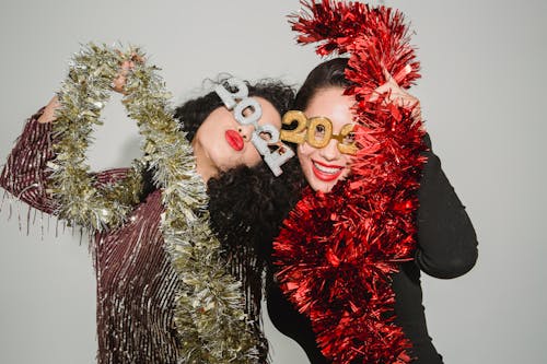 Free Happy women wearing festive dresses and 2021 glasses wrapped with shiny tinsel while celebrating New Year Stock Photo