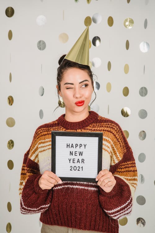 Ethnic woman winking while showing frame with New Year congratulation