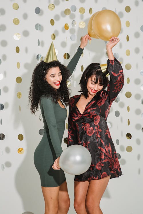 Cheerful women in festive caps with balloons among shiny confetti