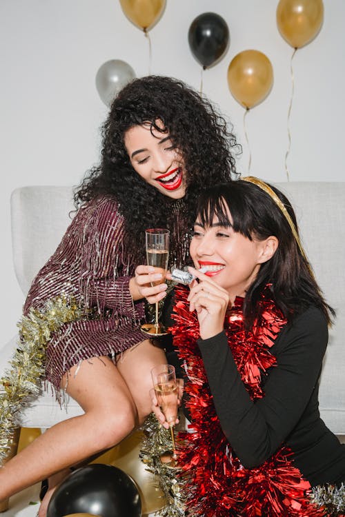 Young happy women smiling with red and golden tinsel while having glasses of champagne