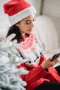 Woman in warm sweater and Santa hat checking smartphone