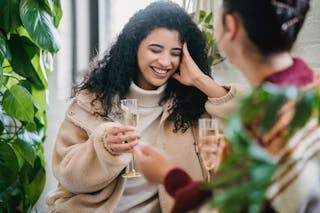 Happy ethnic young woman with glass of champagne laughing