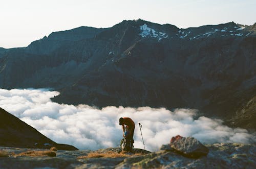 Anonymous traveler packing rucksack while pausing trekking in high rocky mountains covered with clouds