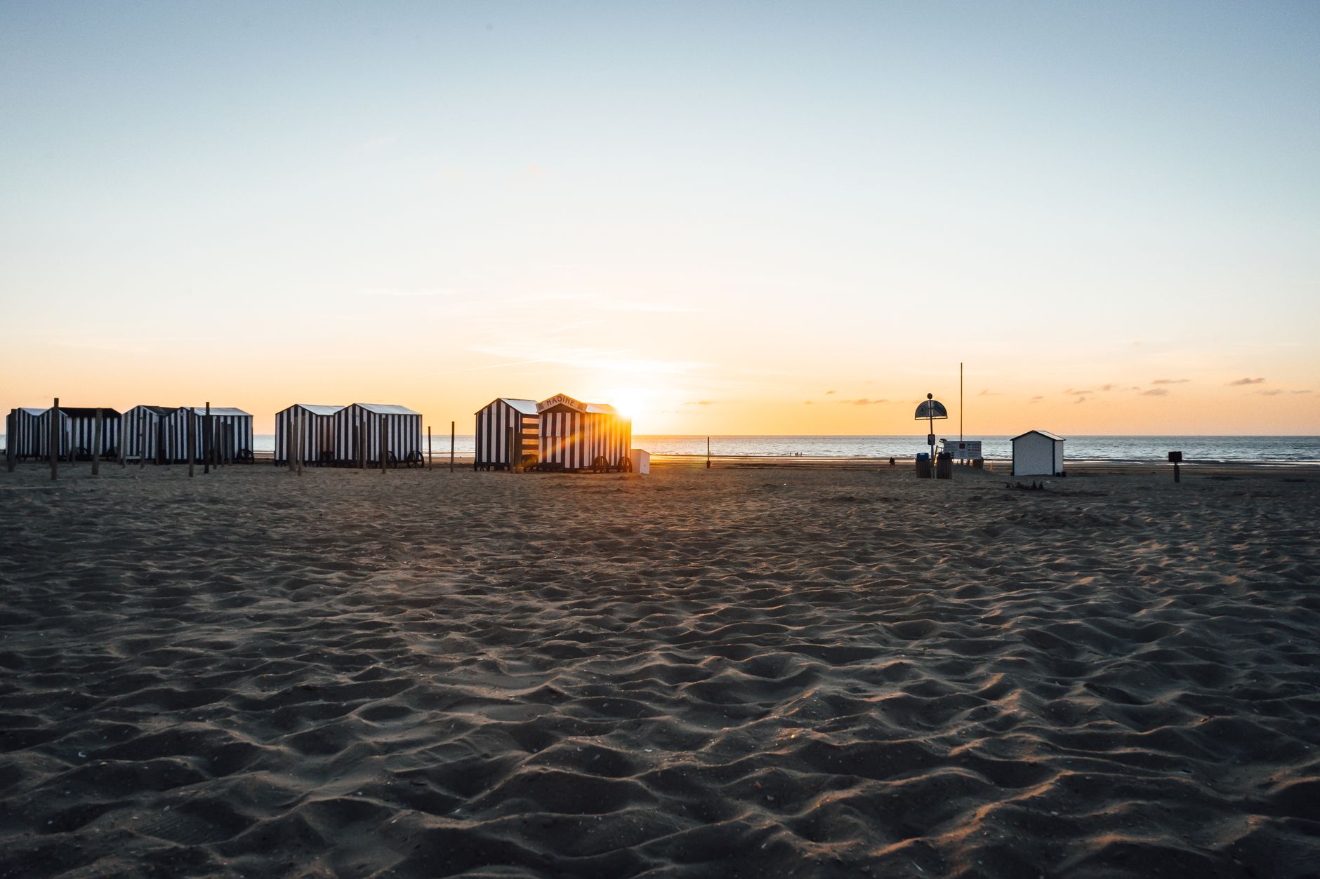 Beautiful sunset view at De Panne Beach, Belgium with striped beach huts and golden sand.