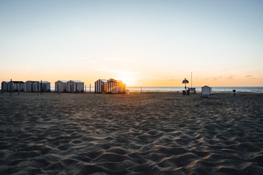 Beautiful sunset view at De Panne Beach, Belgium with striped beach huts and golden sand.