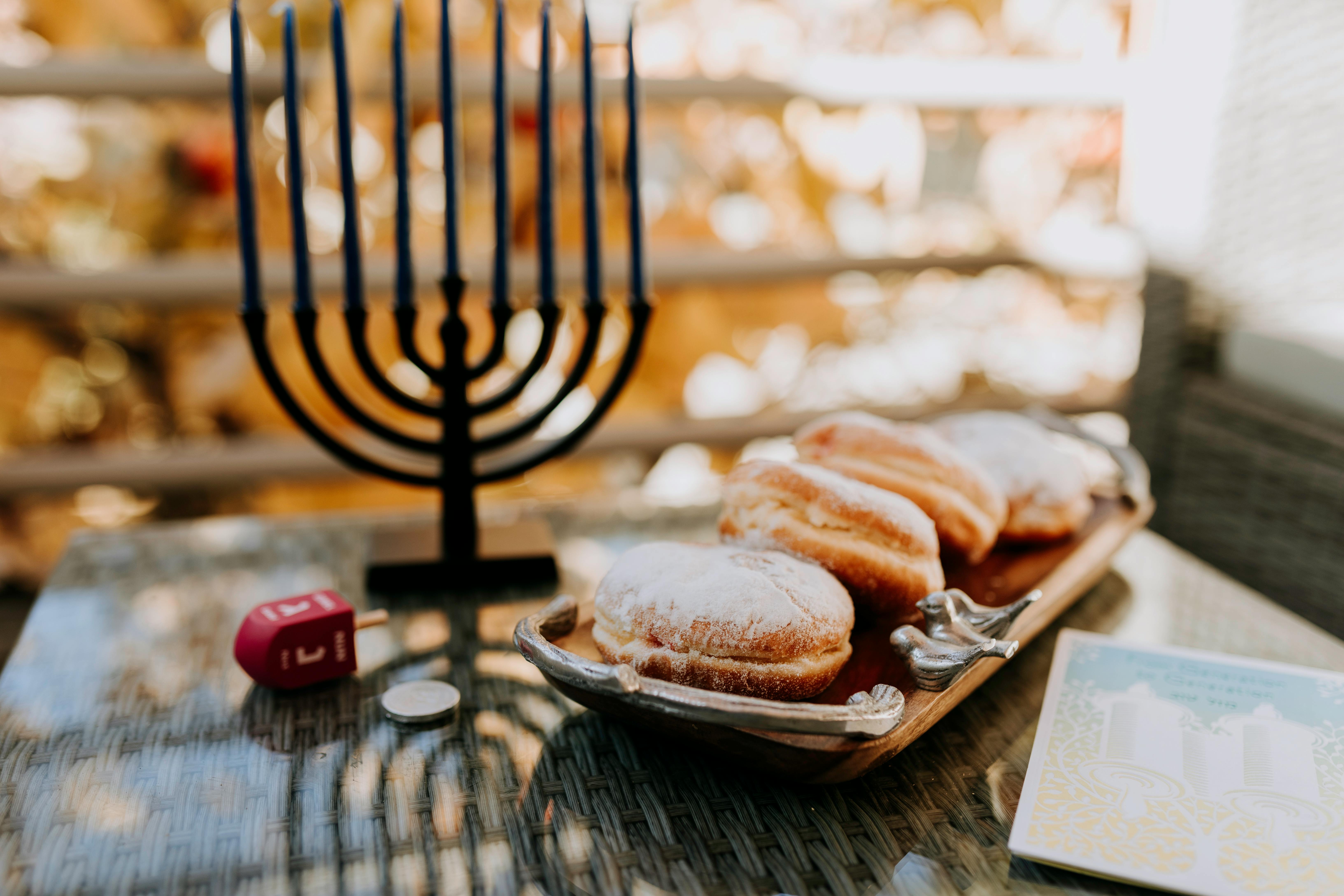 A vibrant Hanukkah scene with a menorah, dreidel, and sufganiyot on a reflective surface.