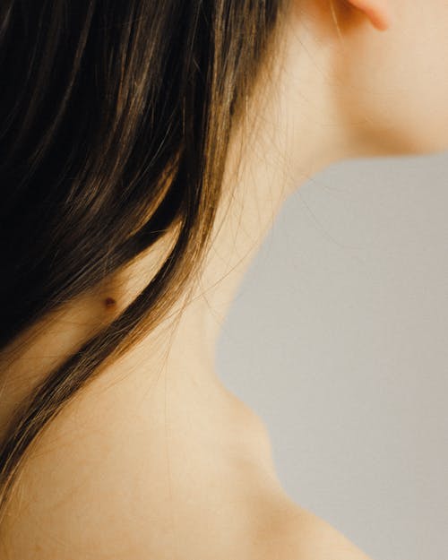 Free Closeup side view of crop unrecognizable young lady with mole on neck with perfect skin under long dark hair on white background Stock Photo