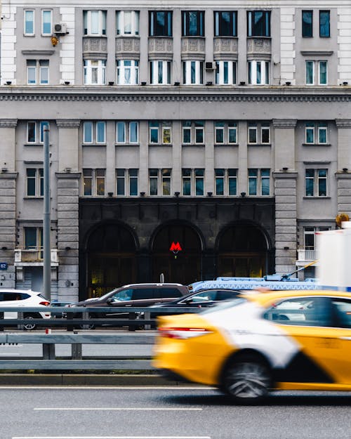 Yellow cabs driving along busy city road past building with subway entrance