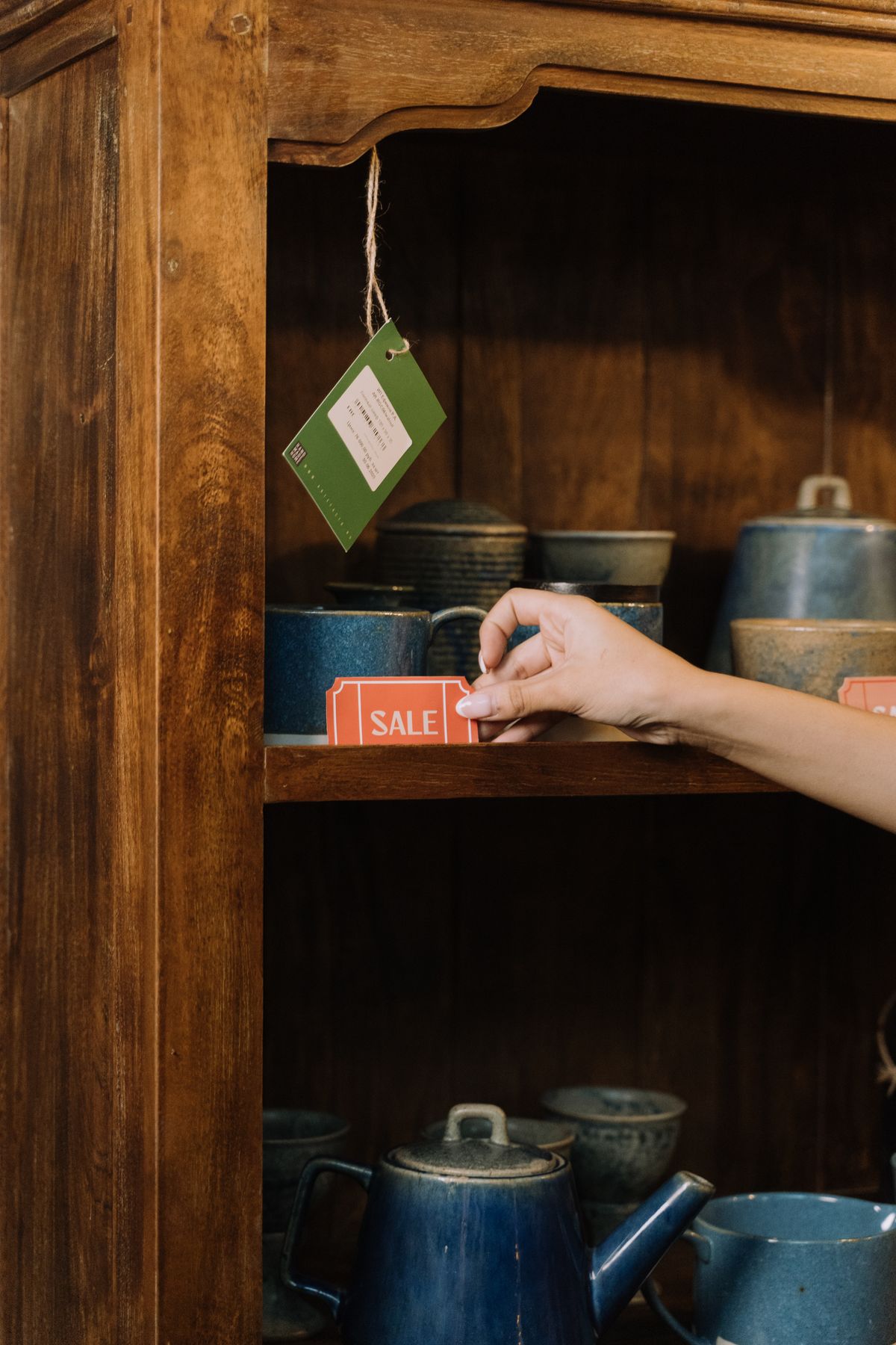 A hand placing a red sale tag on a wooden store shelf