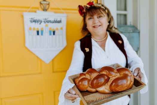 Smiling woman presenting freshly baked traditional challah bread for Hanukkah on a wooden tray.