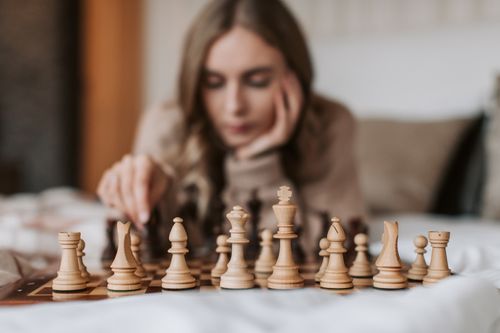 Free Focused woman engages in a thoughtful chess match, planning her next move on a wooden board. Stock Photo