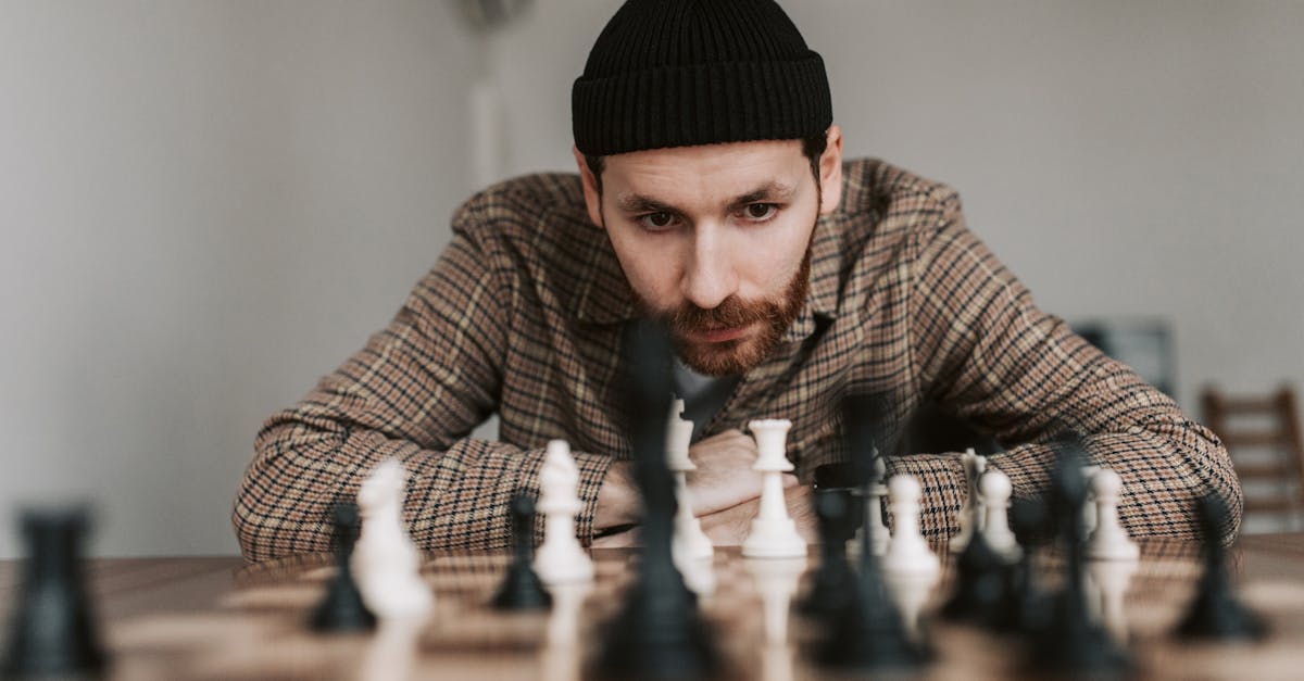 Focused man in beanie plays chess indoors, engaged in strategic thought.