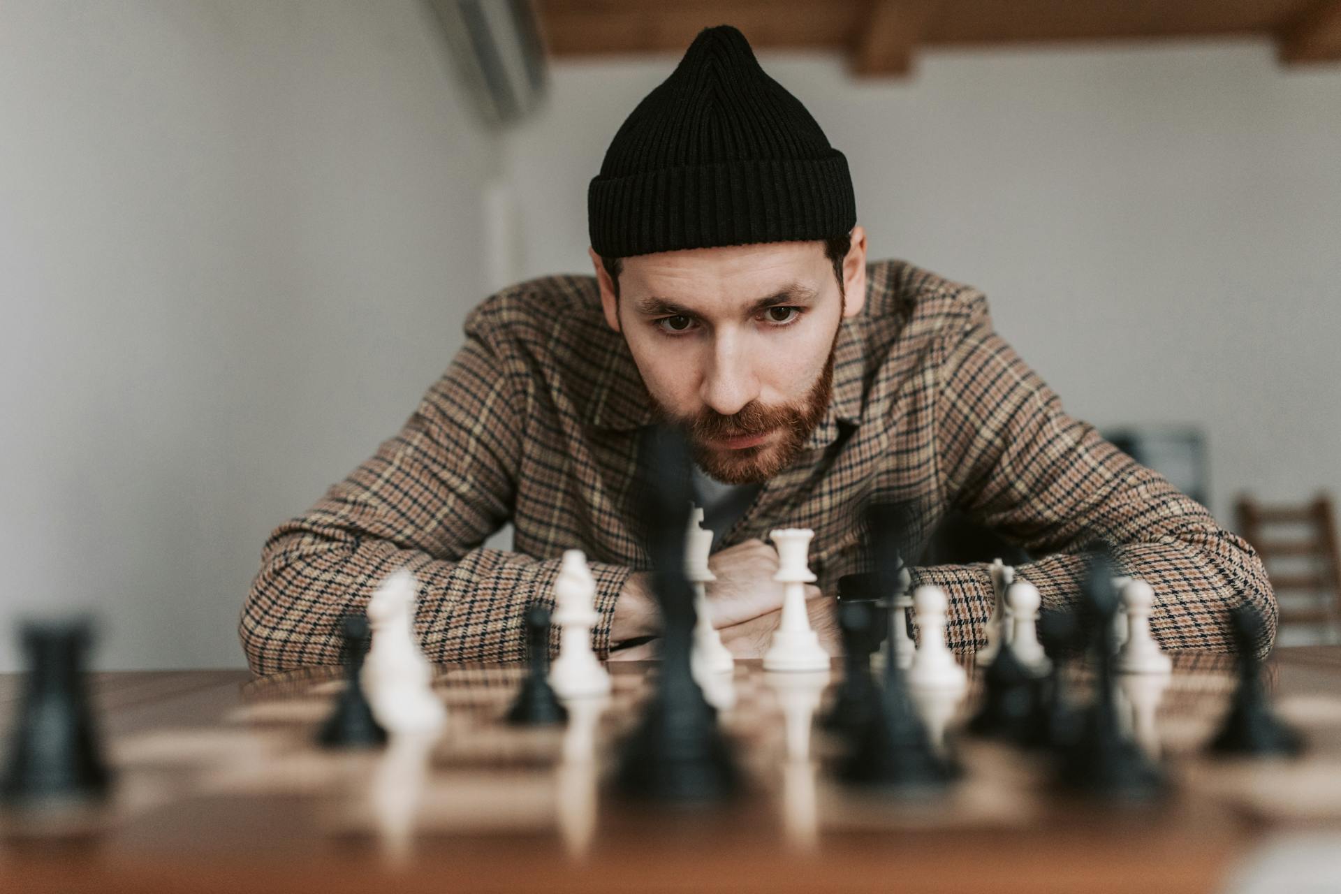 Focused man in beanie plays chess indoors, engaged in strategic thought.