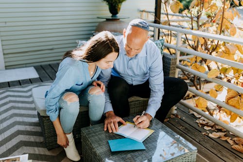 Photo Of Man Writing On A Paper On Top Of Glass Table 