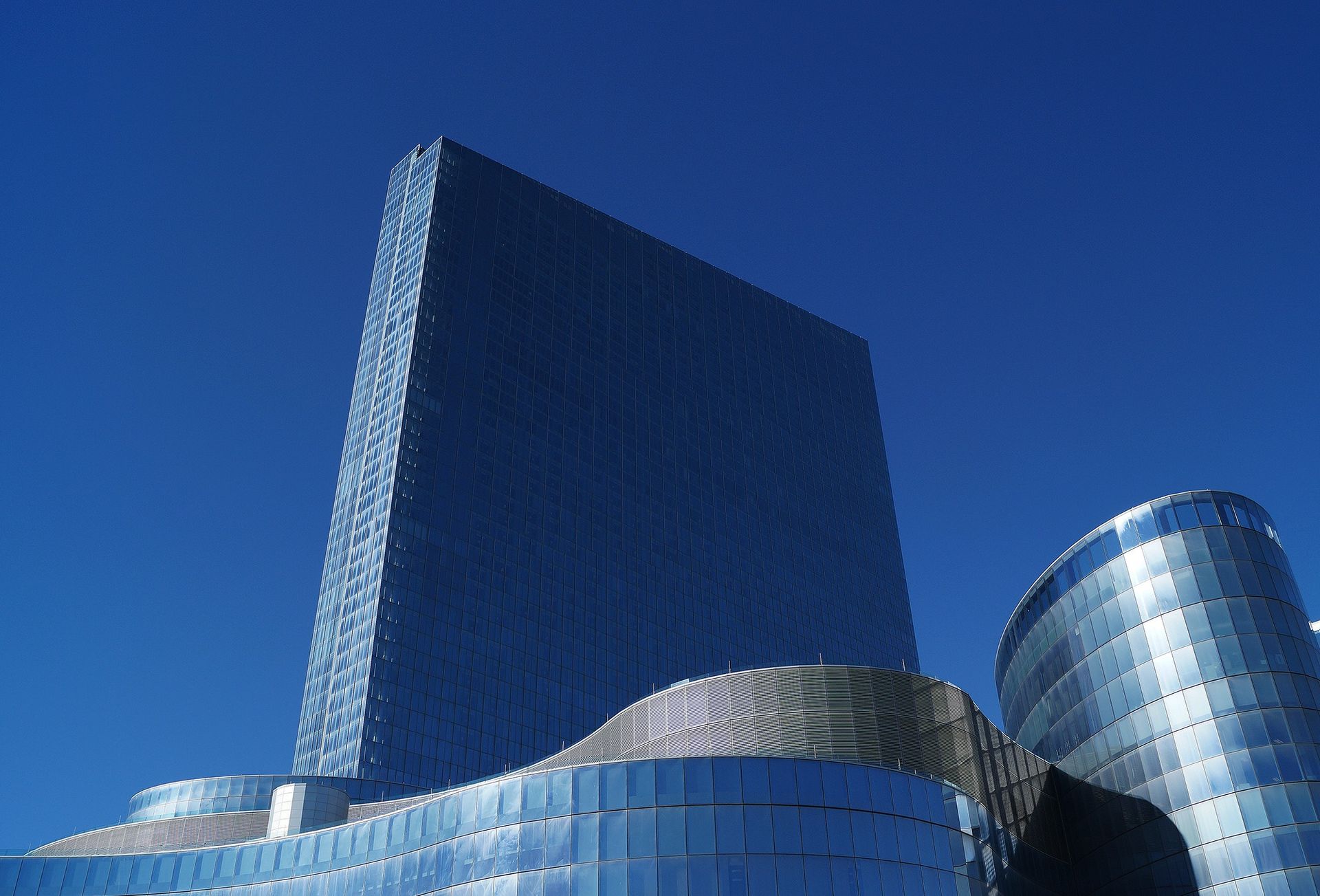 A low-angle shot of a modern skyscraper with glass facade reflecting a clear blue sky.