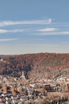 Scenic autumn view of a town with a church, surrounded by colorful forests and hills.