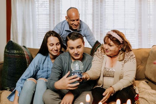 A family gathered together indoors, celebrating Hanukkah with a snow globe and lighted candles.