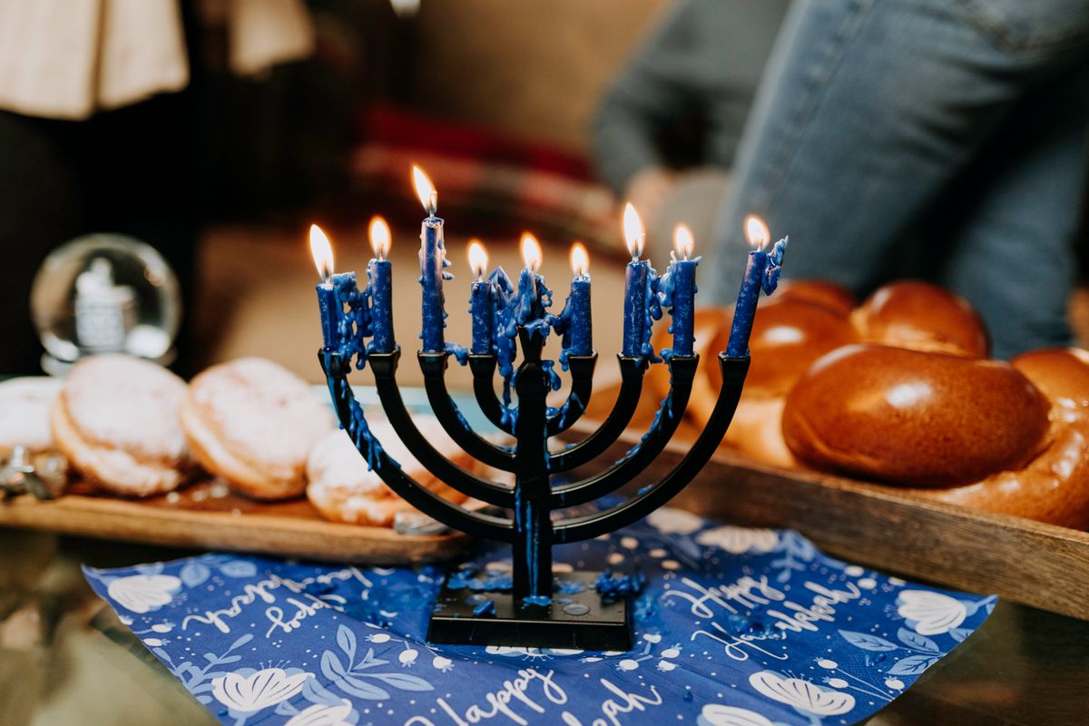 A lit Hanukkah menorah with sufganiyot and challah on a festive table
