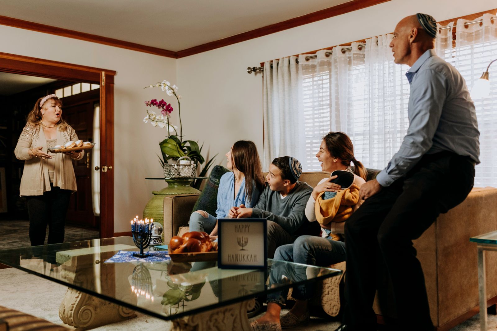 Family talking in a sunny living room, a menorah and challah on the coffee table