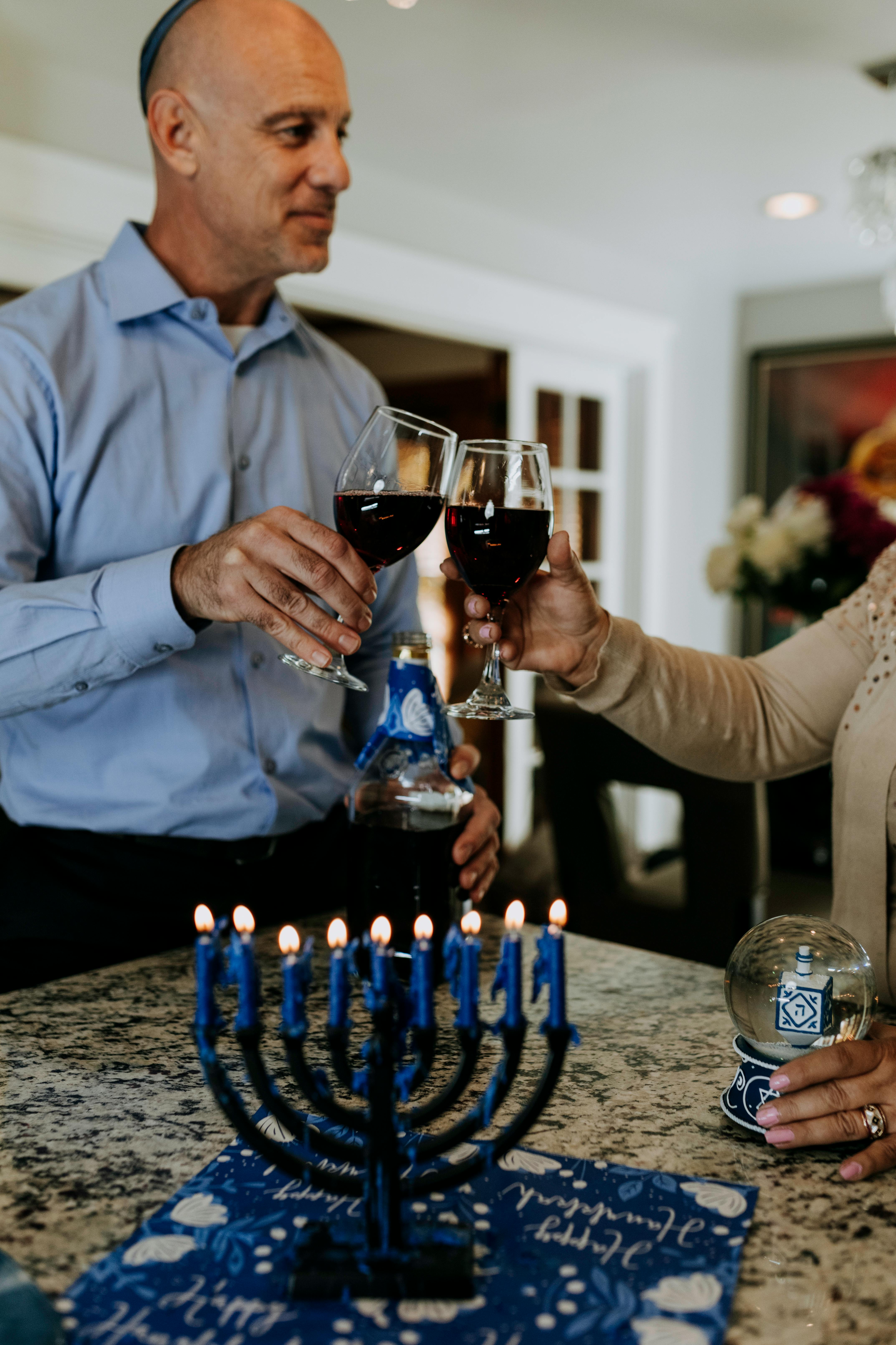 Adults celebrating Hanukkah with toasting red wine over a lit menorah.