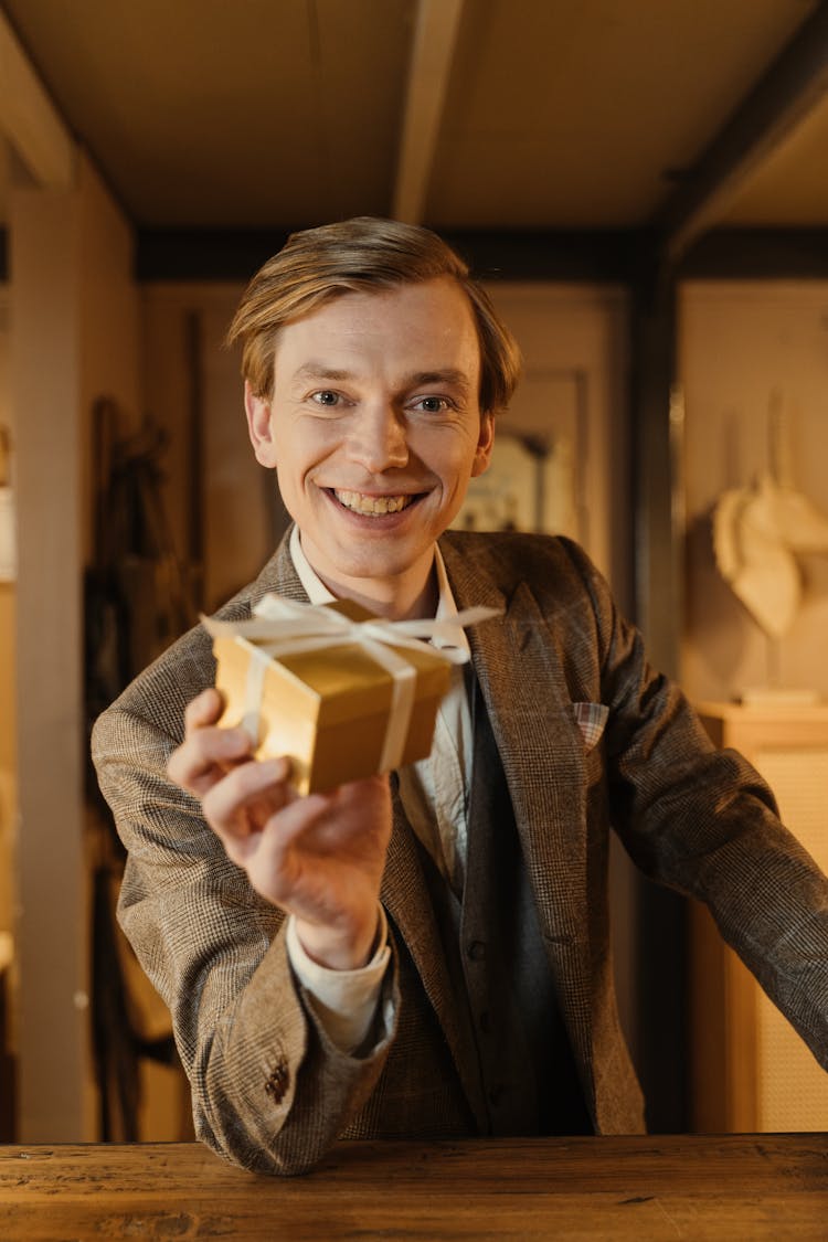 Man In Gray Blazer Holding A Gold Box With Ribbon