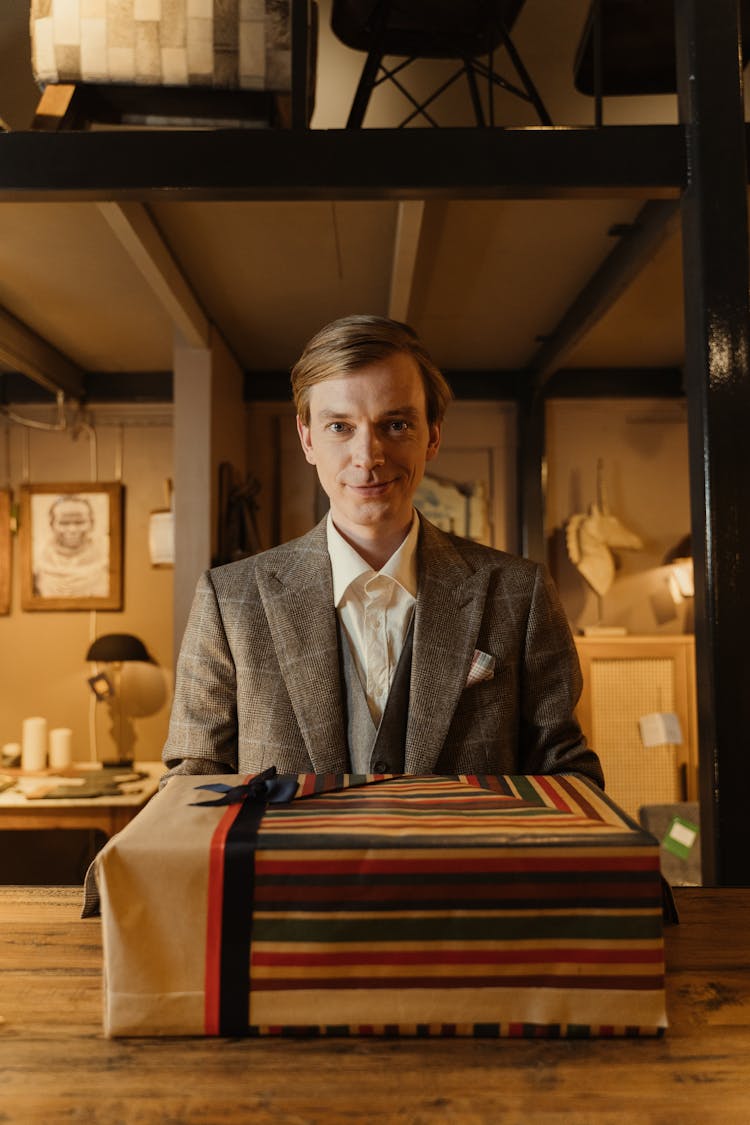 A Man Standing Behind A Desk With A Wrapped Gift Box