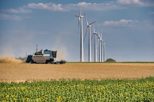 Machine Harvesting and Wind Turbine Under White Clouds and Blue Sky