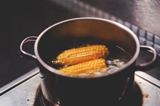 Two cobs of corn boiling in a stainless steel pot on a stove, creating a cozy kitchen scene.