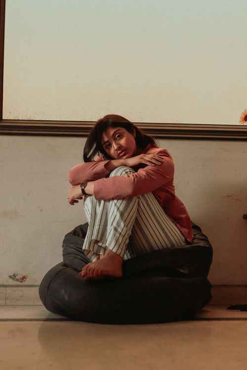 Free Calm female with dark hair in casual clothes sitting and embracing knees on bean bag chair in room Stock Photo