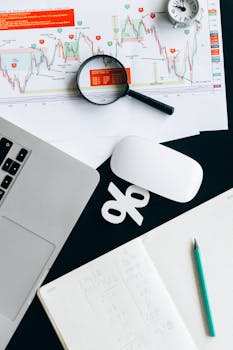 Top view of financial documents with magnifying glass, laptop, and notebook.
