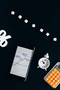 Flat lay of financial market analysis with smartphone, chart, and alarm clock against black background.