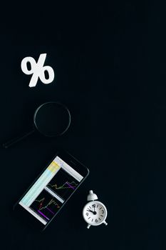 Smartphone displaying stock market charts with a magnifying glass and clock on a black background.