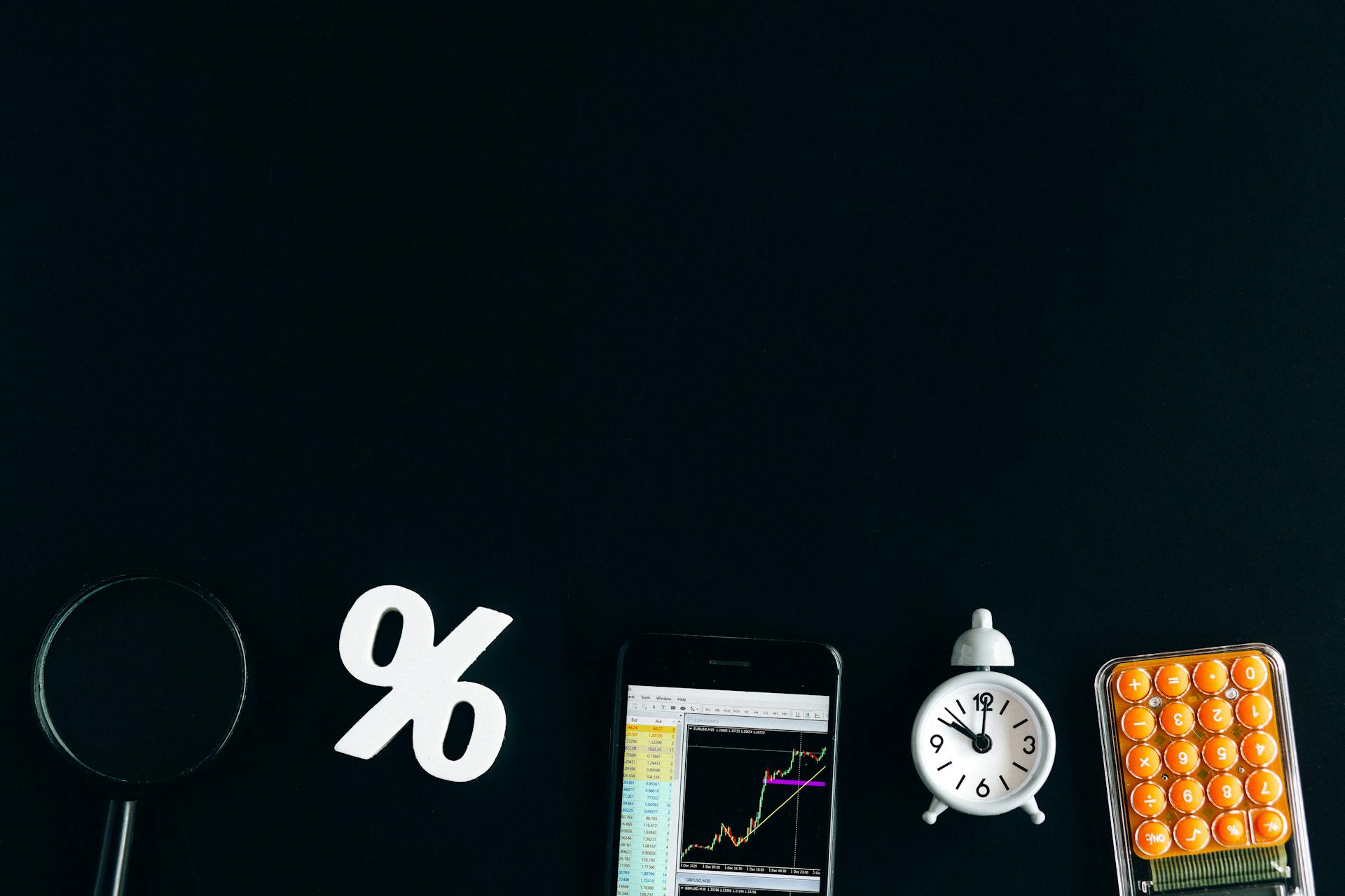 Flat lay of financial analysis tools including phone, clock, and calculator on black background.