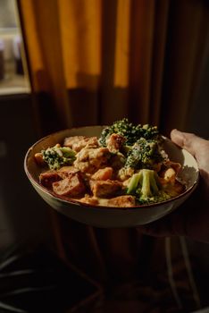 A delicious bowl of broccoli and tofu, captured in warm indoor lighting, perfect for a cozy meal setting.