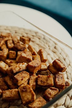 Close-up of crispy baked tofu cubes in a glass dish on a woven mat, perfect for vegan recipes.