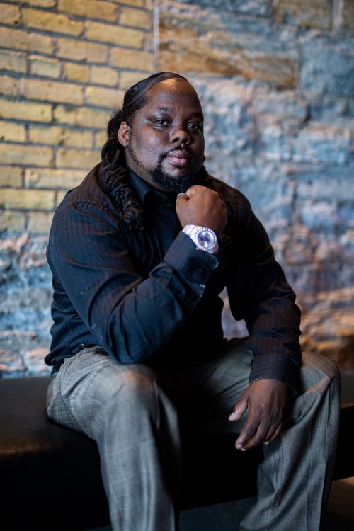 Free Portrait of a man in black attire posing confidently against a textured brick wall. Stock Photo